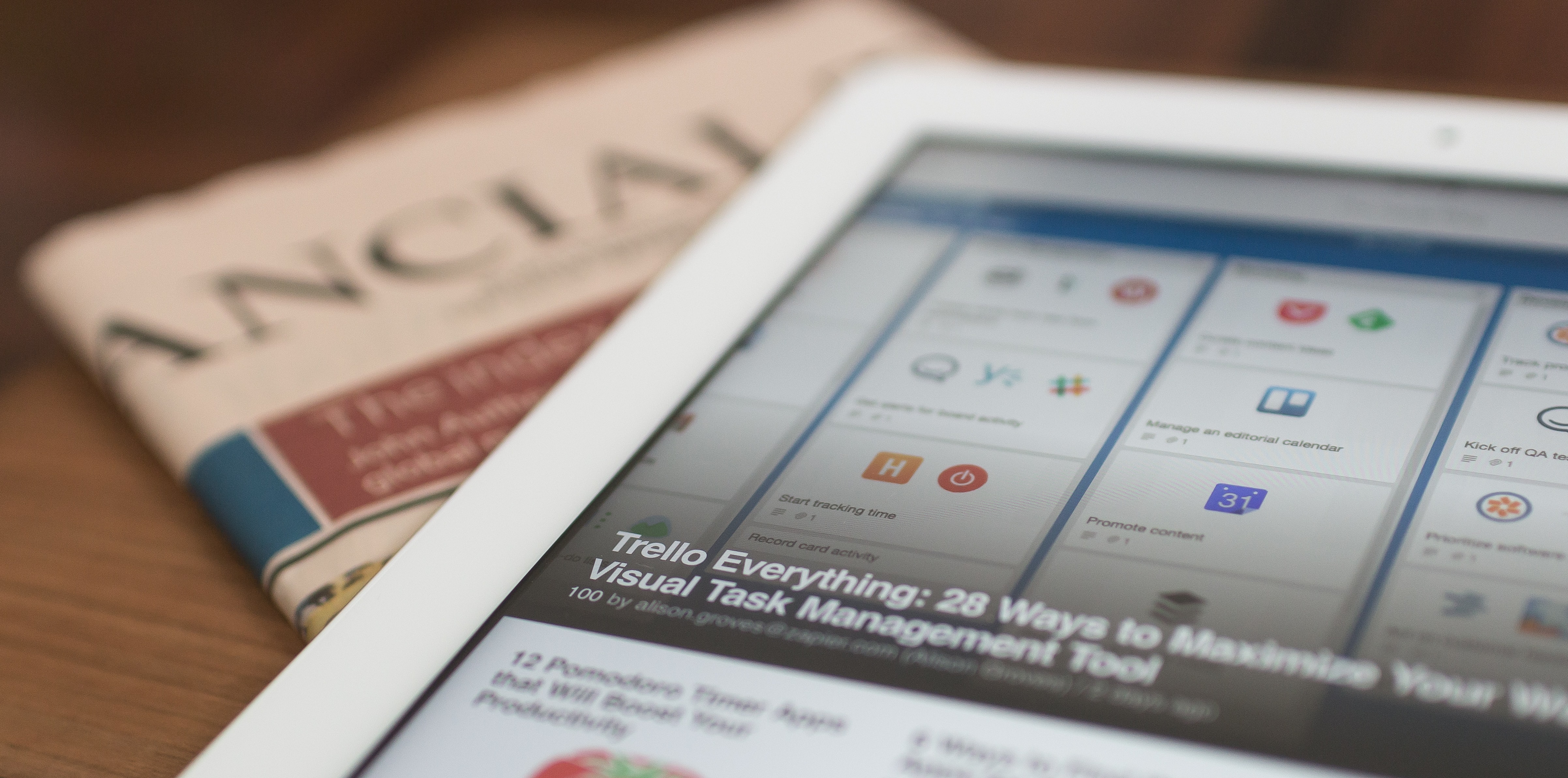 Protopian Times Image Sitting on top of a wooden executive desk is a white apple iPad with Protopian Times Blog on the screen. Out of focus, and under the iPad is a folded financial times newspaper with the title only showing the right side of the light pink newspaper with the title showing “ANCIAL” in capital letters facing up.